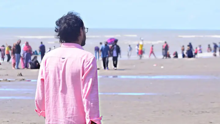 A man in a pink shirt looking out over a busy beach