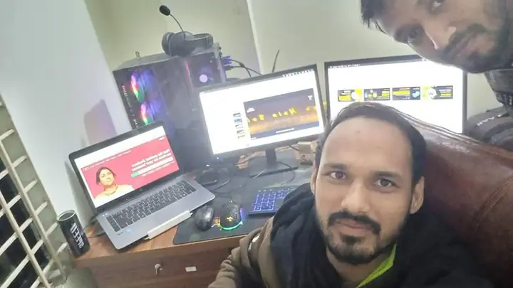 Two team members at a workstation with several screens